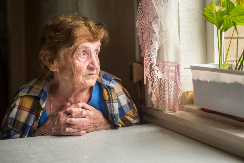 Old lonely woman sitting near the window in his house.