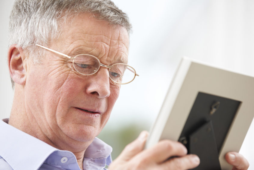 Unhappy Senior Man Looking At Photo In Frame