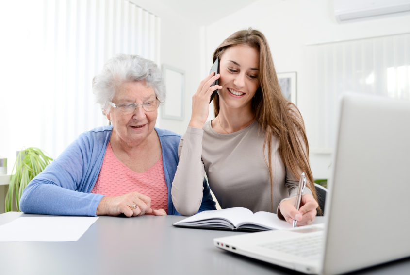 young woman helping old senior woman doing paperwork and administrative procedures with laptop computer at home
