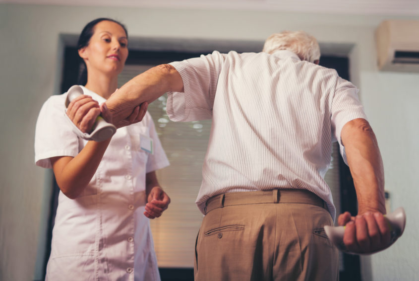 Senior man with dumbbells in rehab with a physiotherapist