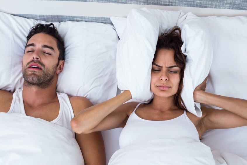 Woman blocking ears while man snoring on bed Chrapanie a zdrowie